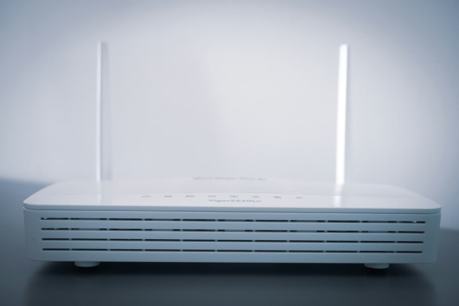 Hvid trådløs router med to antenner på et bord foran en lys væg